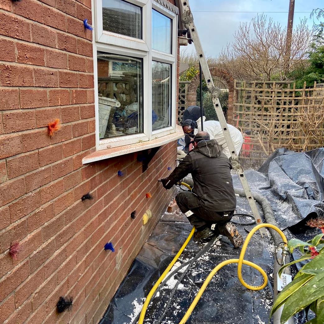 Cutaway diagram of cavity wall insulation being blown into a double brick wall through a small drilled hole