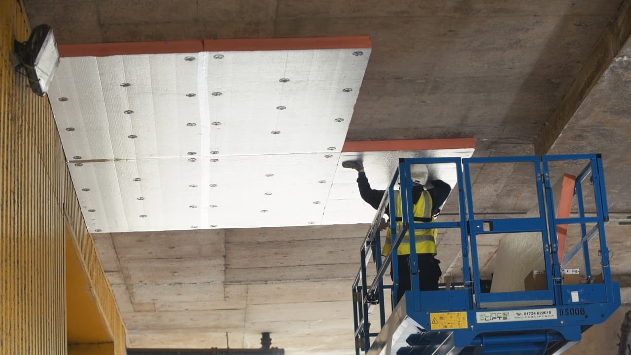 1 Stop Insulation installer fixing soffit insulation panels under a concrete slab from a scissor lift